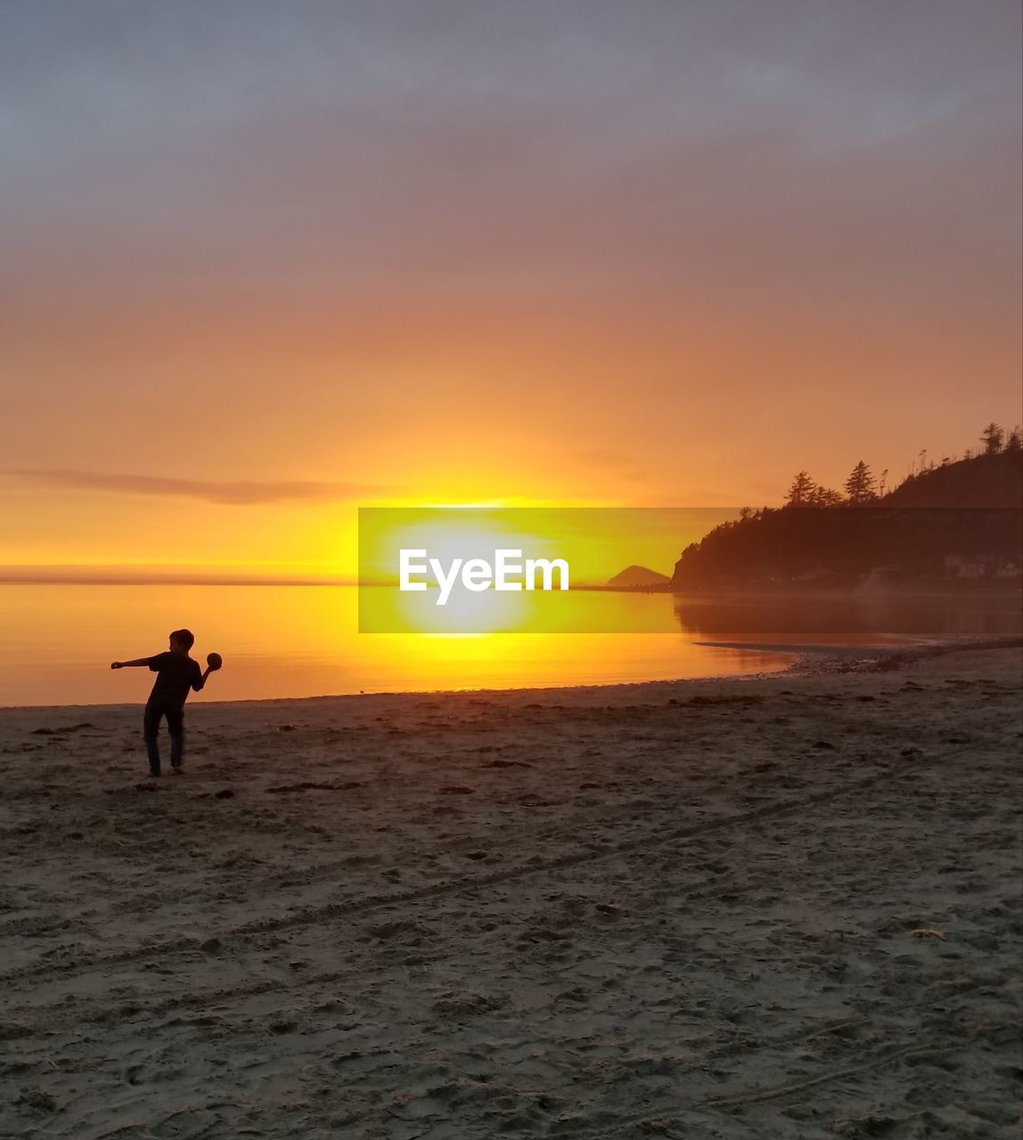 Silhouette boy at beach against sky during sunset