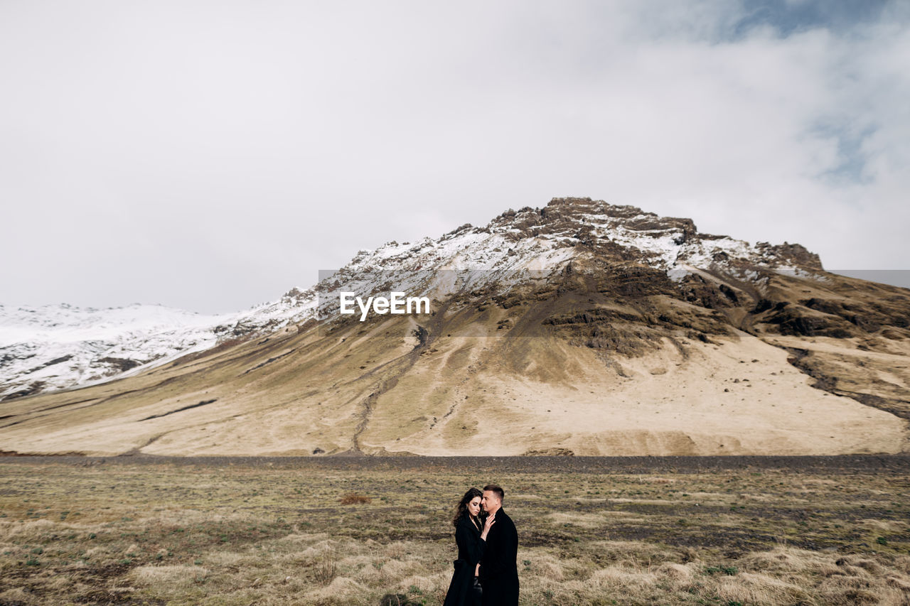 WOMAN STANDING ON MOUNTAIN AGAINST SKY