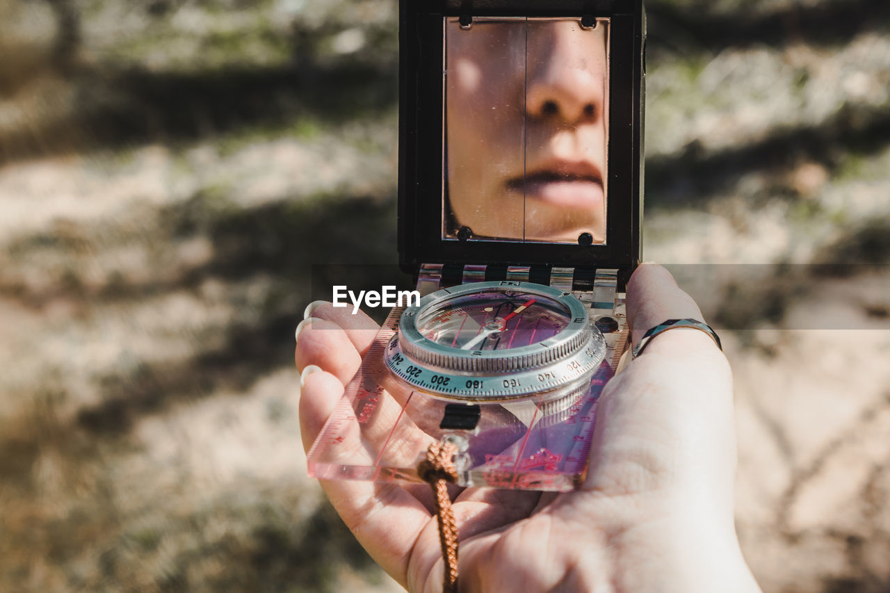 Close-up of young woman holding compass with reflection in mirror