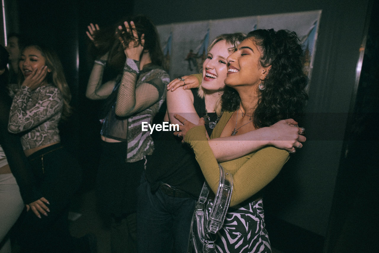 Cheerful young women embracing while enjoying at nightclub