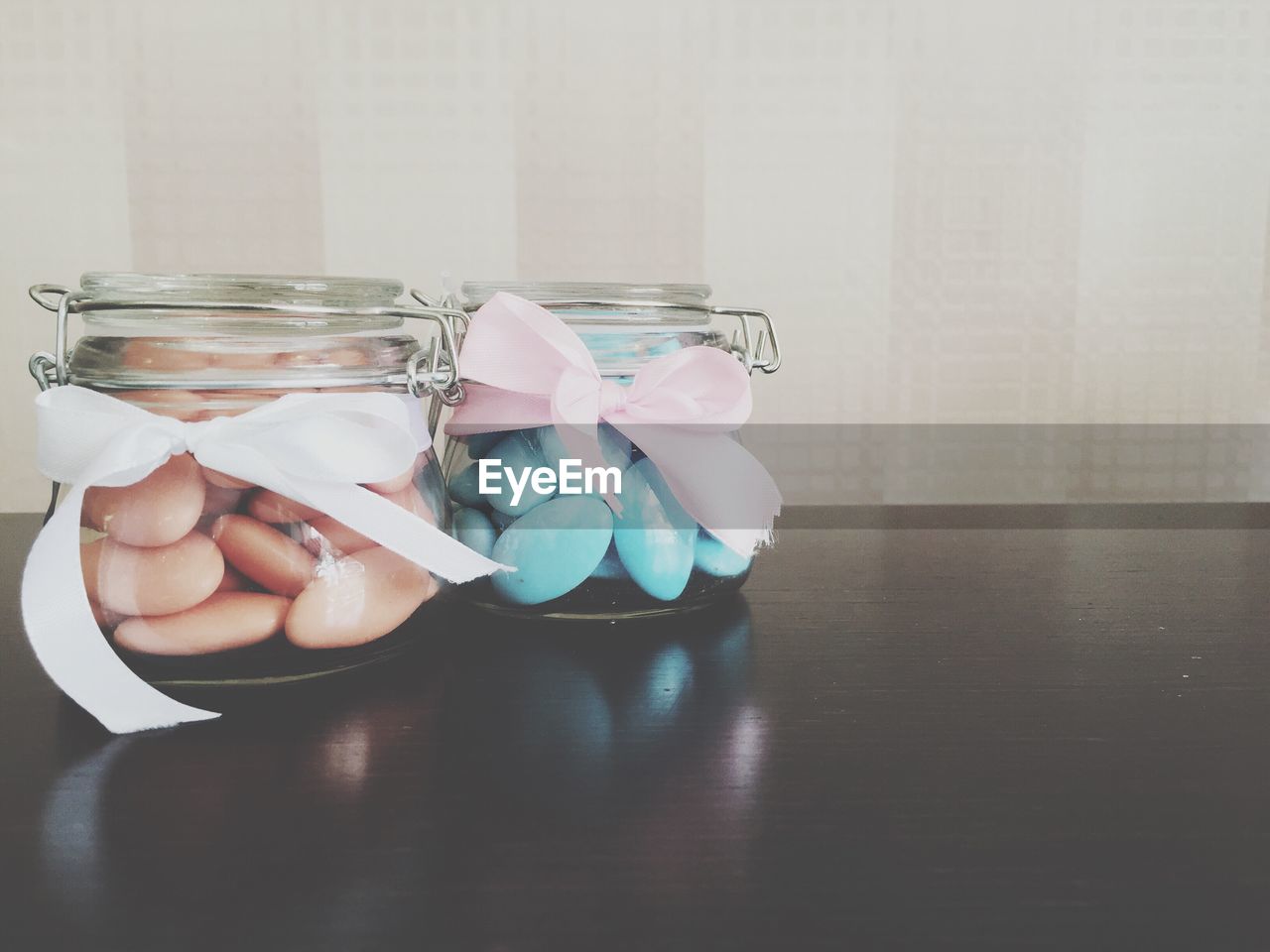 Food in glass containers with ribbons on table against wall