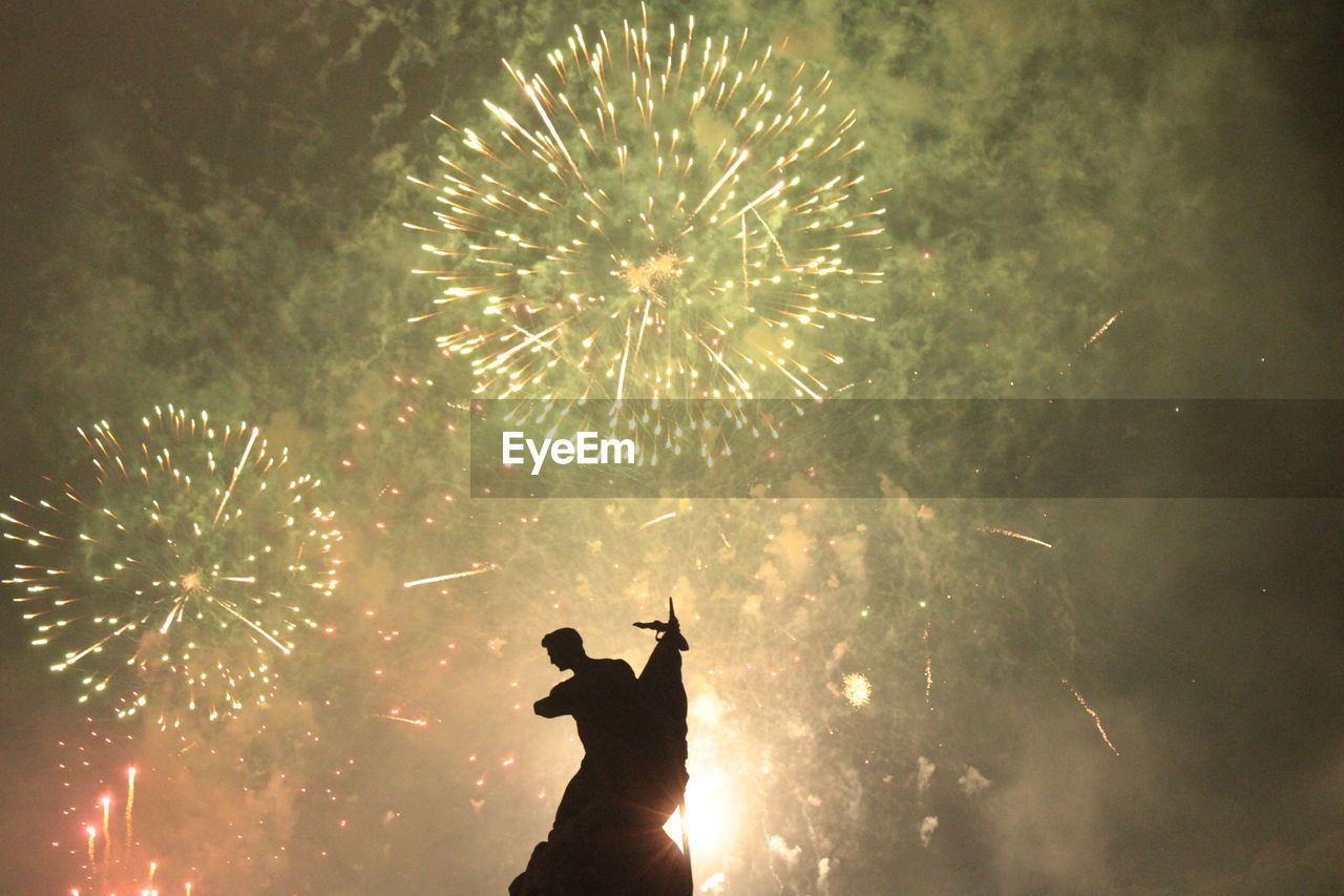 low angle view of people watching fireworks against sky at night