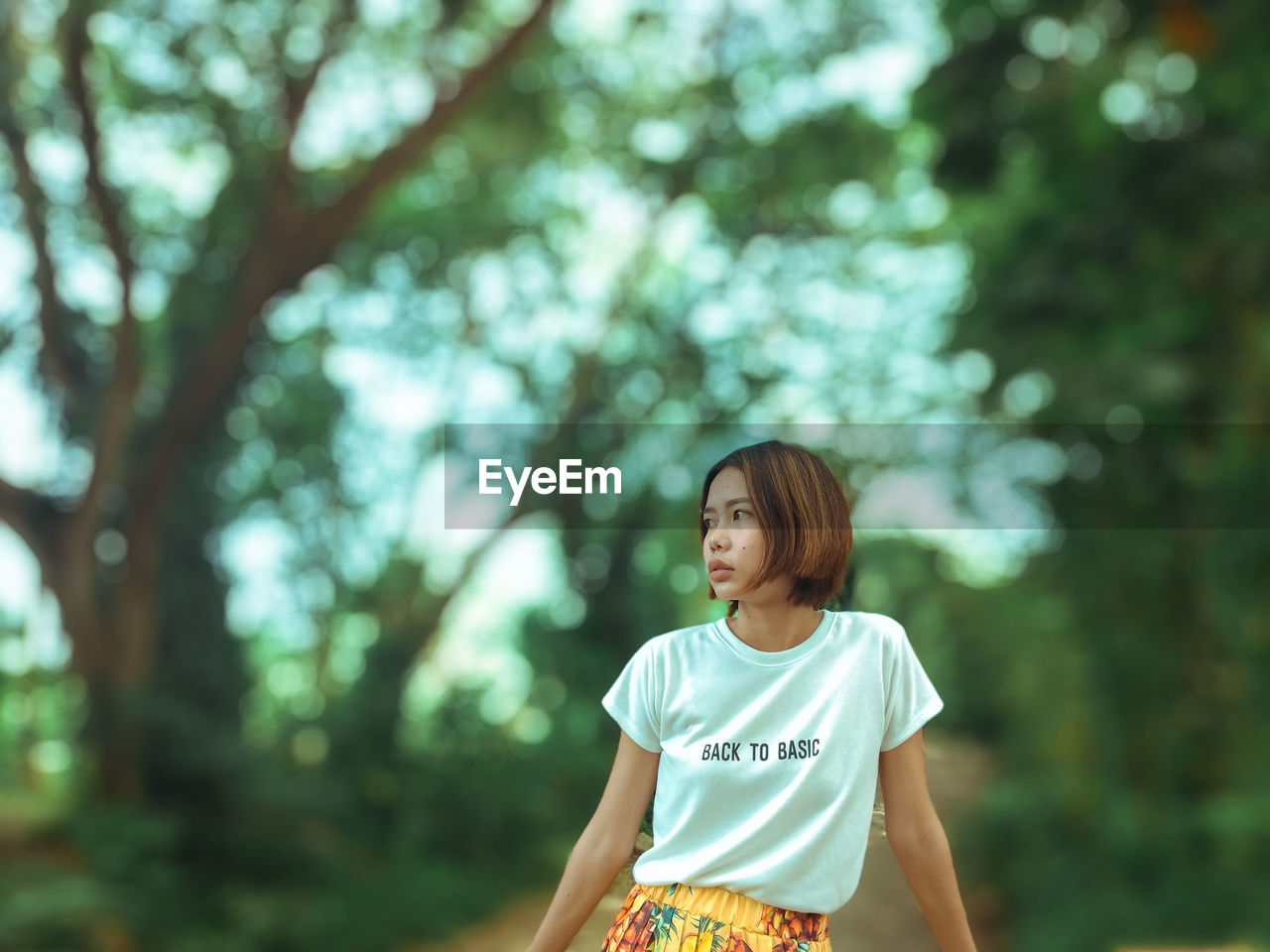 WOMAN LOOKING AWAY WHILE STANDING ON TREE