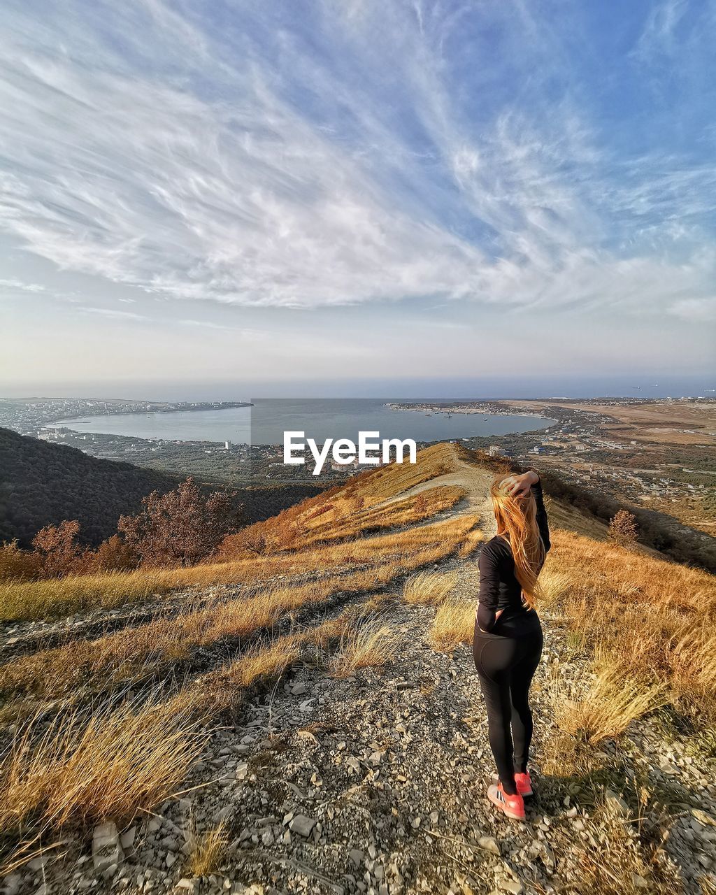 REAR VIEW OF WOMAN STANDING AGAINST SKY DURING SUNNY DAY