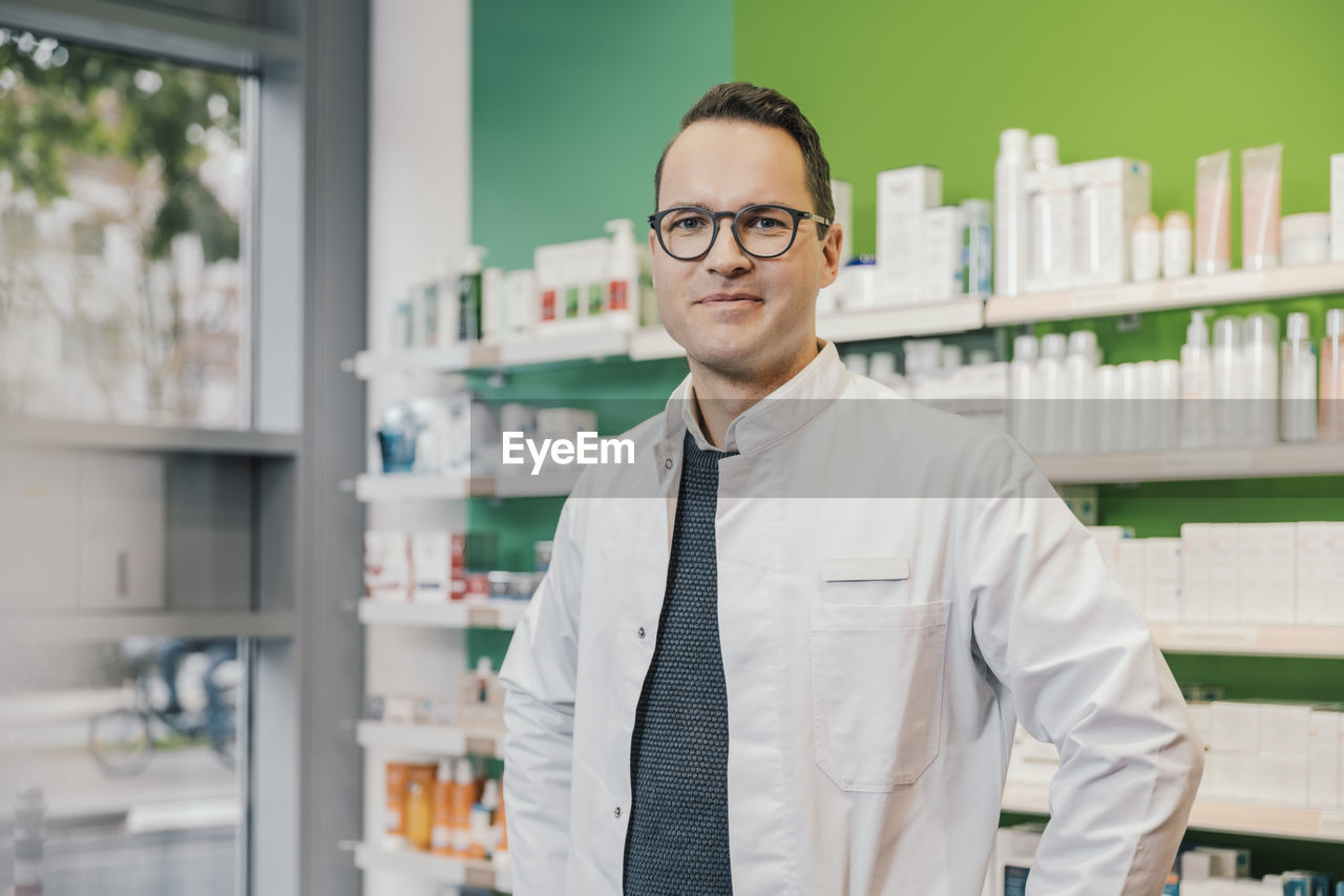 Smiling pharmacist wearing lab coat while standing in chemist shop