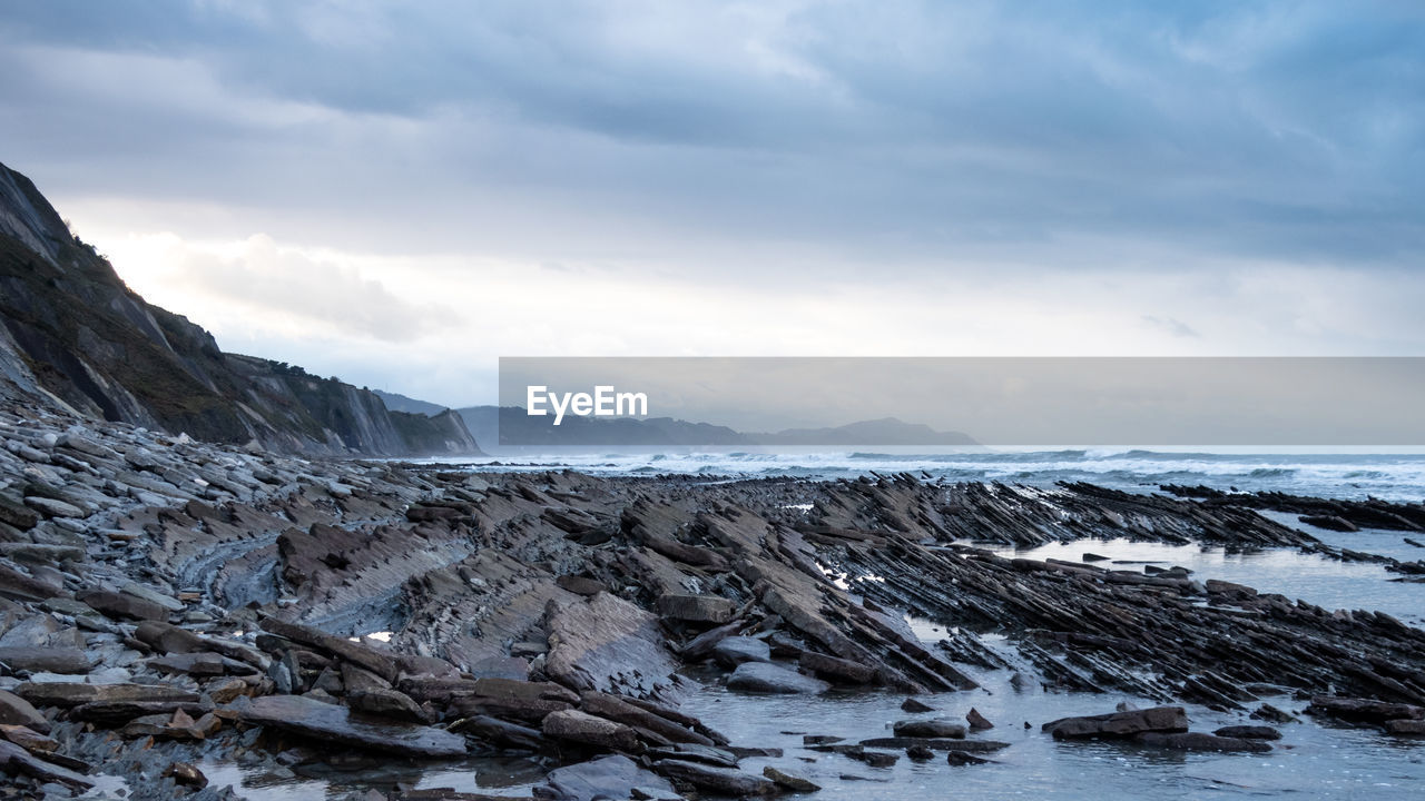 Panoramic view of flysch cliff rock structures at basque sea against sky