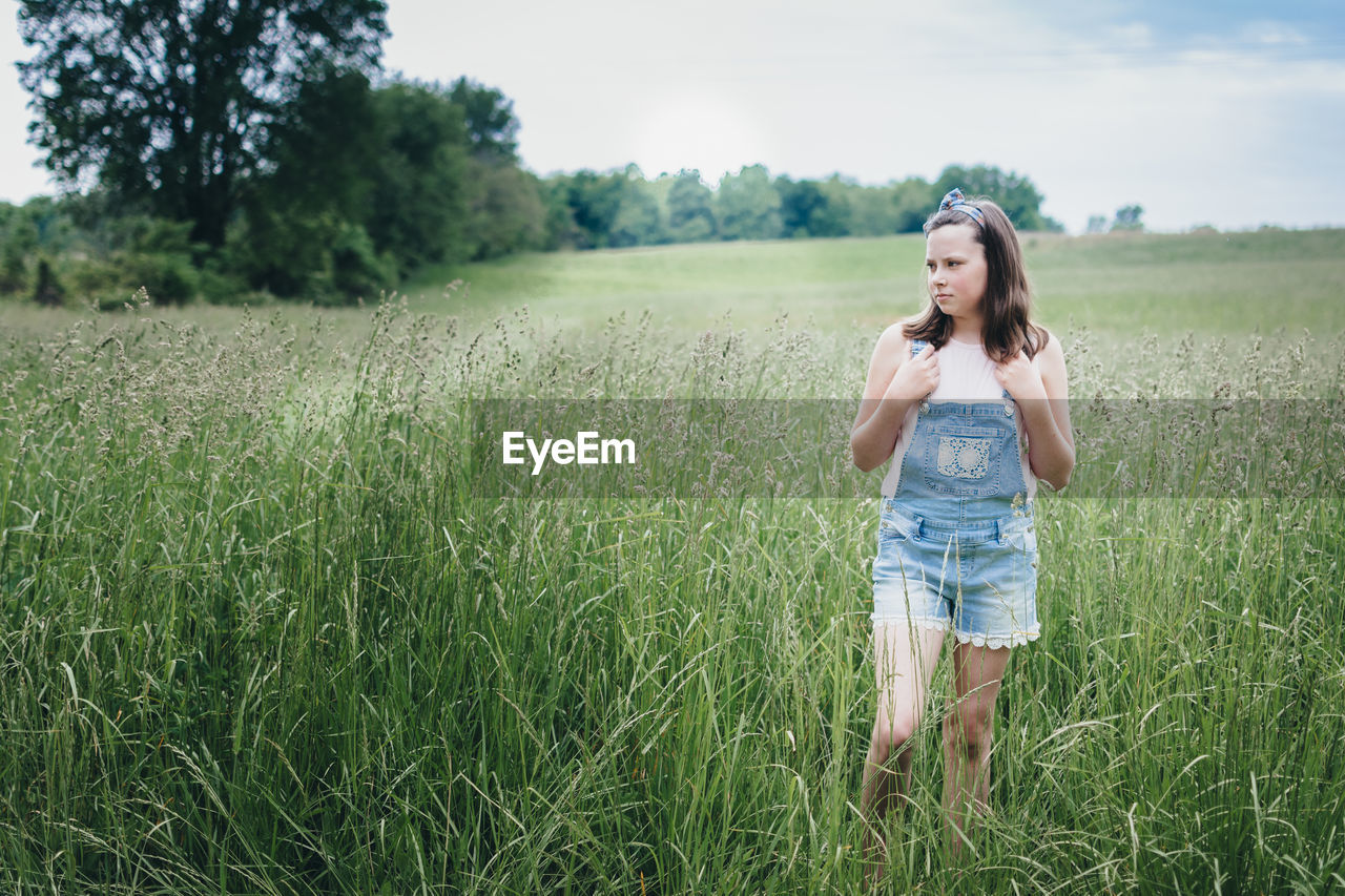 Girl standing in a grassy praire on a summer day.