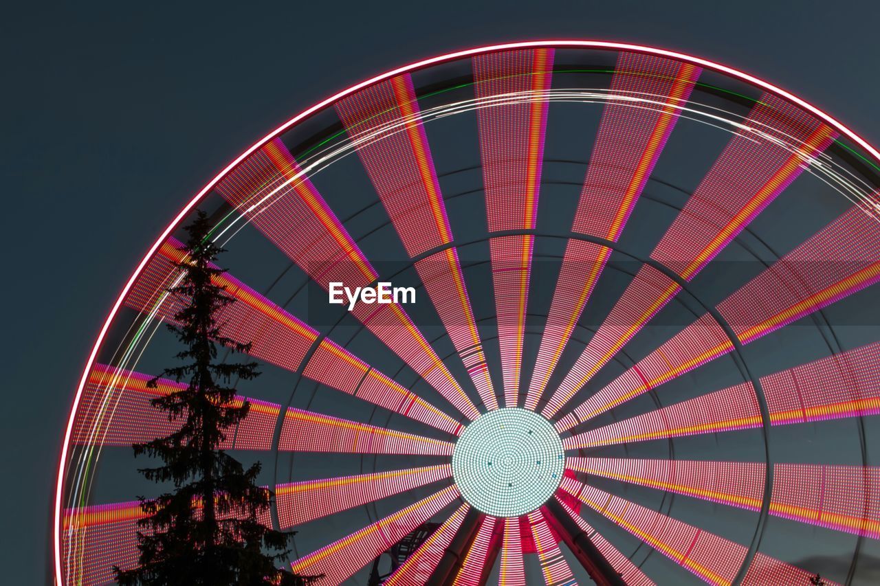 Low angle view of illuminated ferris wheel and tree against sky