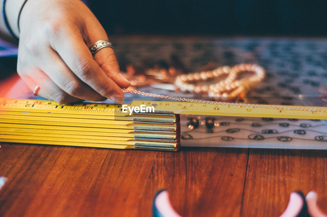 Cropped image of woman measuring chain on wooden table