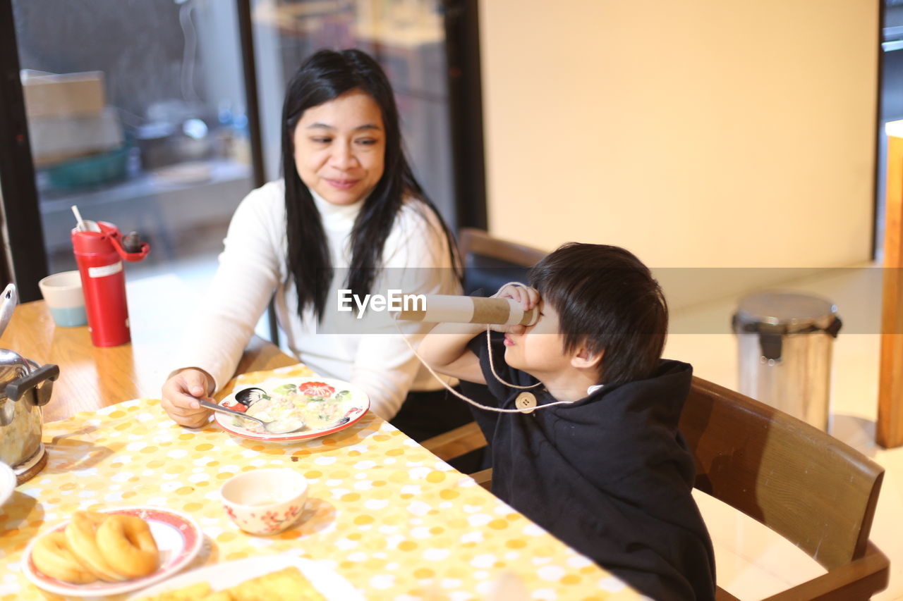 Mother and son having food while sitting at table
