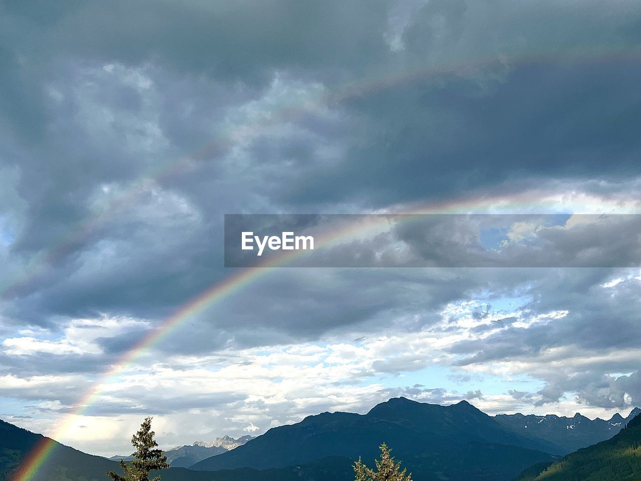 rainbow, sky, cloud, mountain, beauty in nature, scenics - nature, environment, nature, landscape, mountain range, multi colored, dramatic sky, tree, tranquility, no people, tranquil scene, idyllic, storm, plant, land, outdoors, day, travel destinations, non-urban scene, sunlight, overcast, forest, travel, cloudscape, sunbeam, natural phenomenon, storm cloud, mountain peak