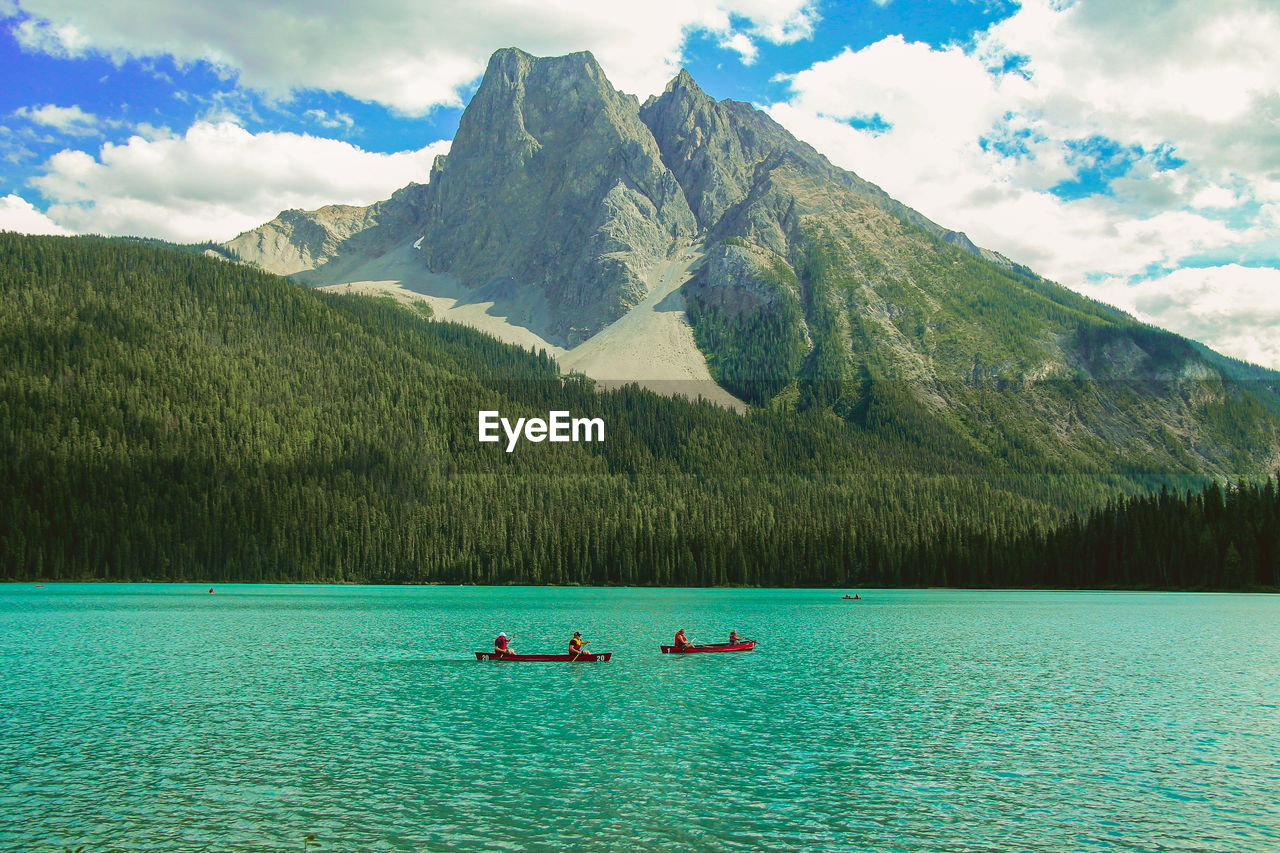 People rowing boat against grassy mountain in emerald lake at yoho national park