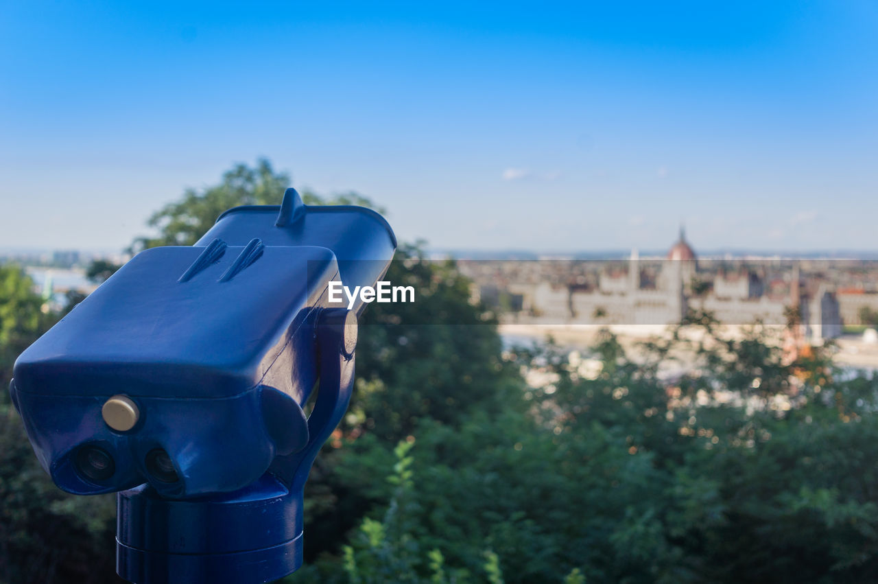 Coin-operated binoculars in city against sky