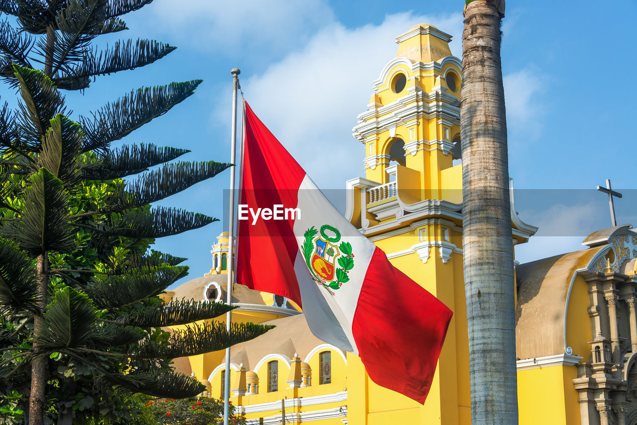 Low angle view of peruvian flag against yellow historic building against sky