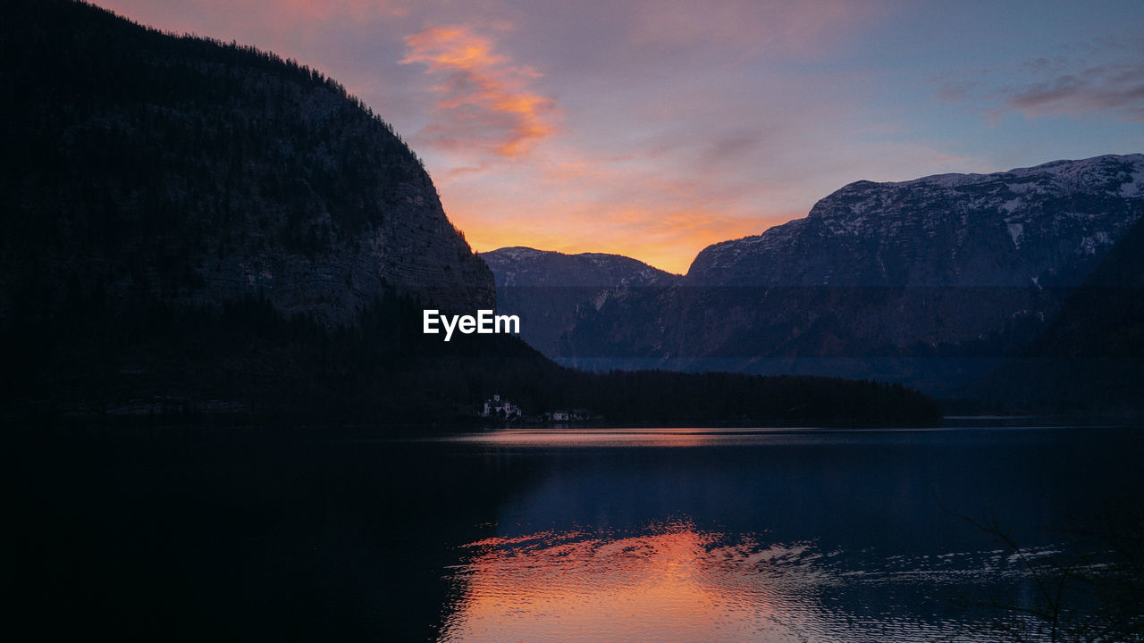 Scenic view of lake by mountains against sky during sunset