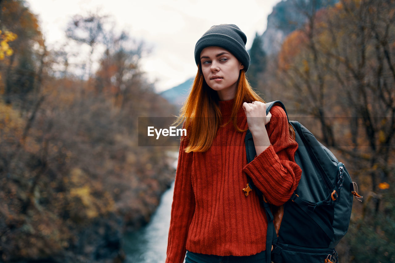 YOUNG WOMAN STANDING AGAINST TREES DURING AUTUMN