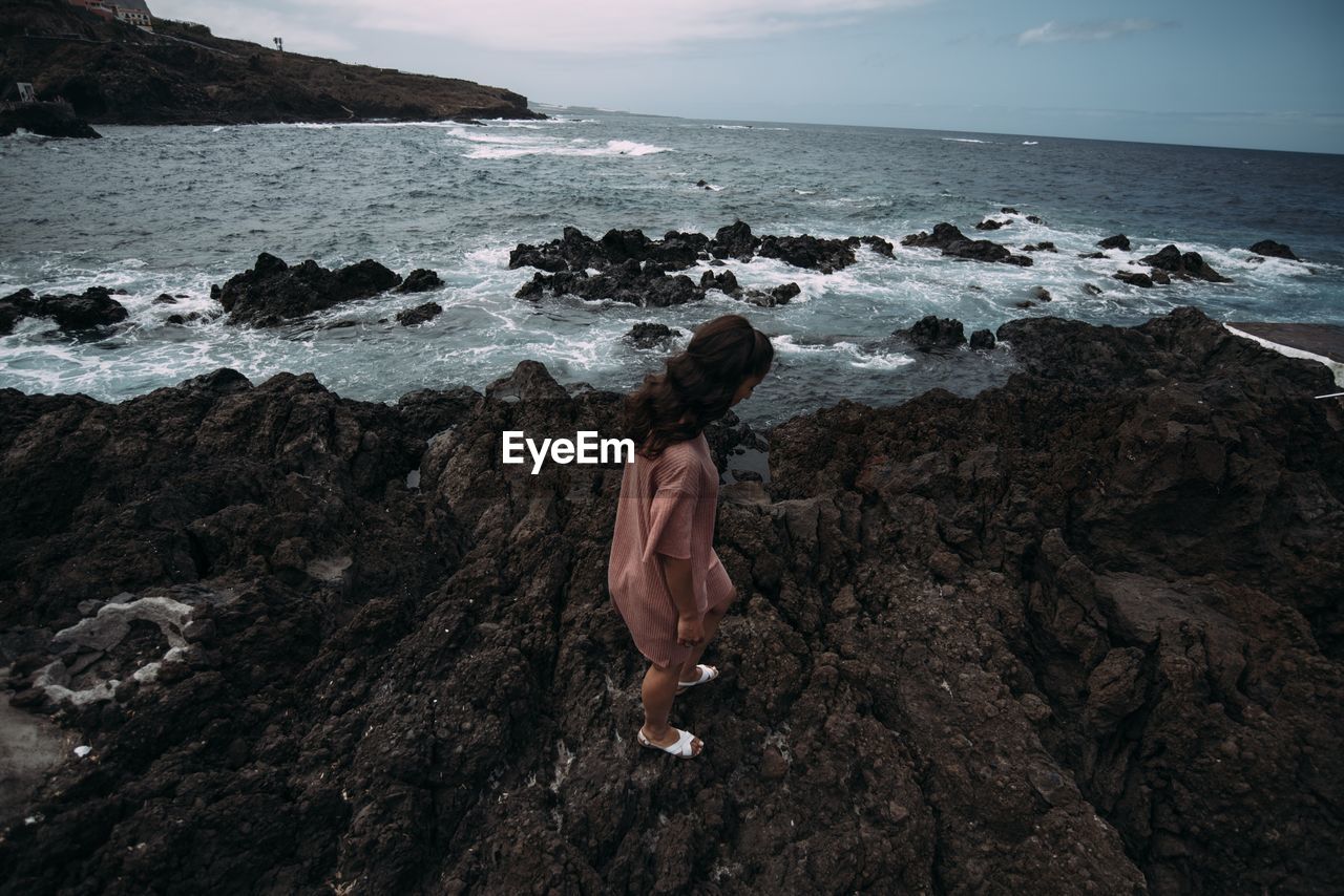 WOMAN STANDING ON ROCK AT BEACH