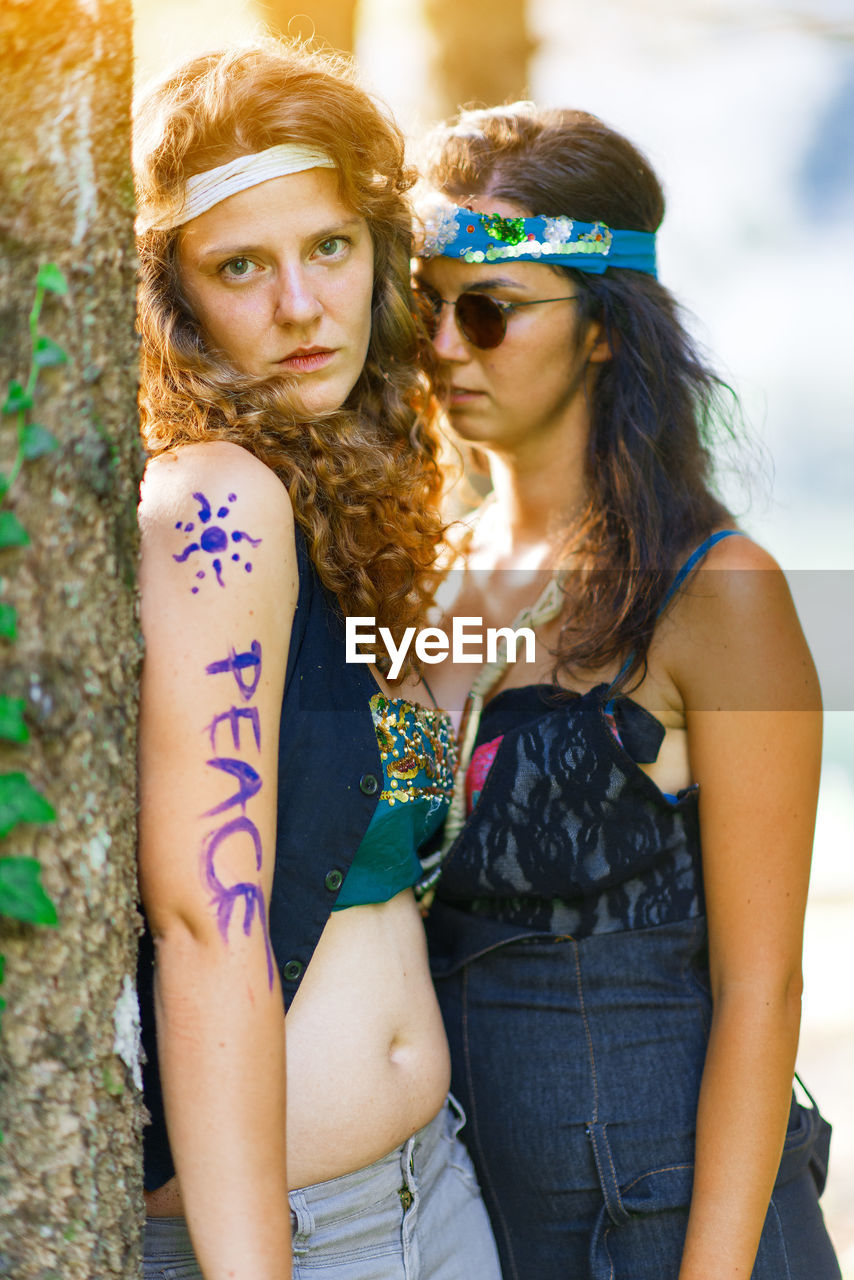 Portrait of lesbian couple standing by tree trunk