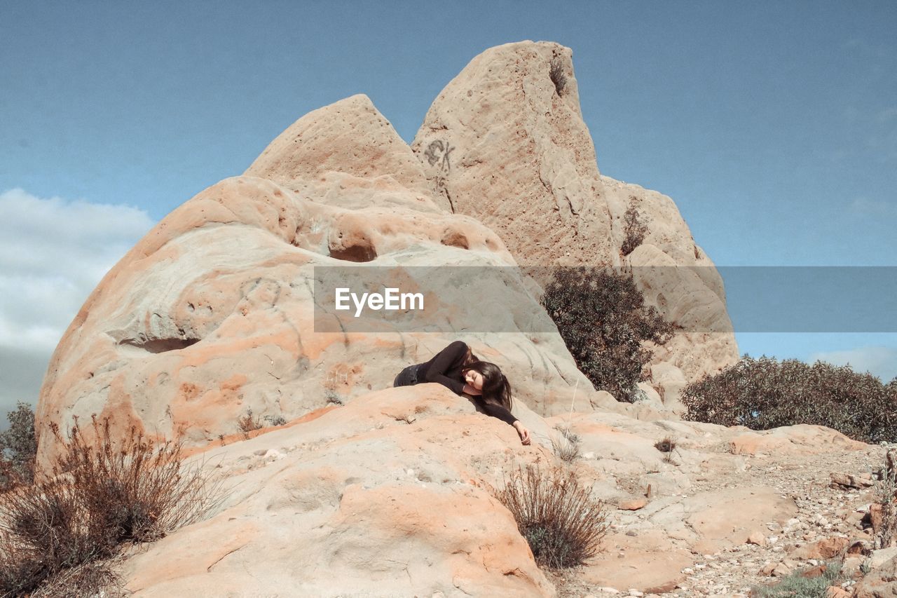 Woman lying on rock at desert during sunny day