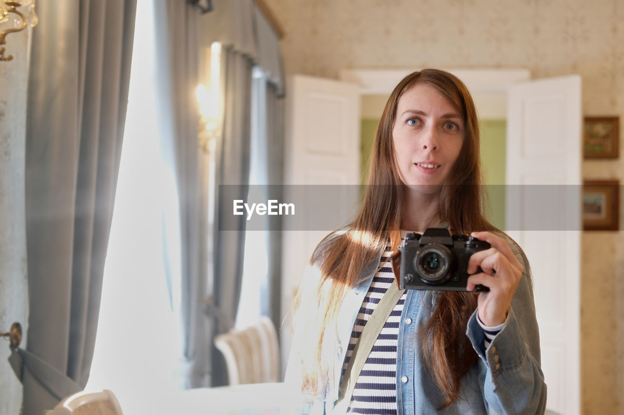 A girl with long hair, in jeans, takes a selfie on the camera, in the mirror