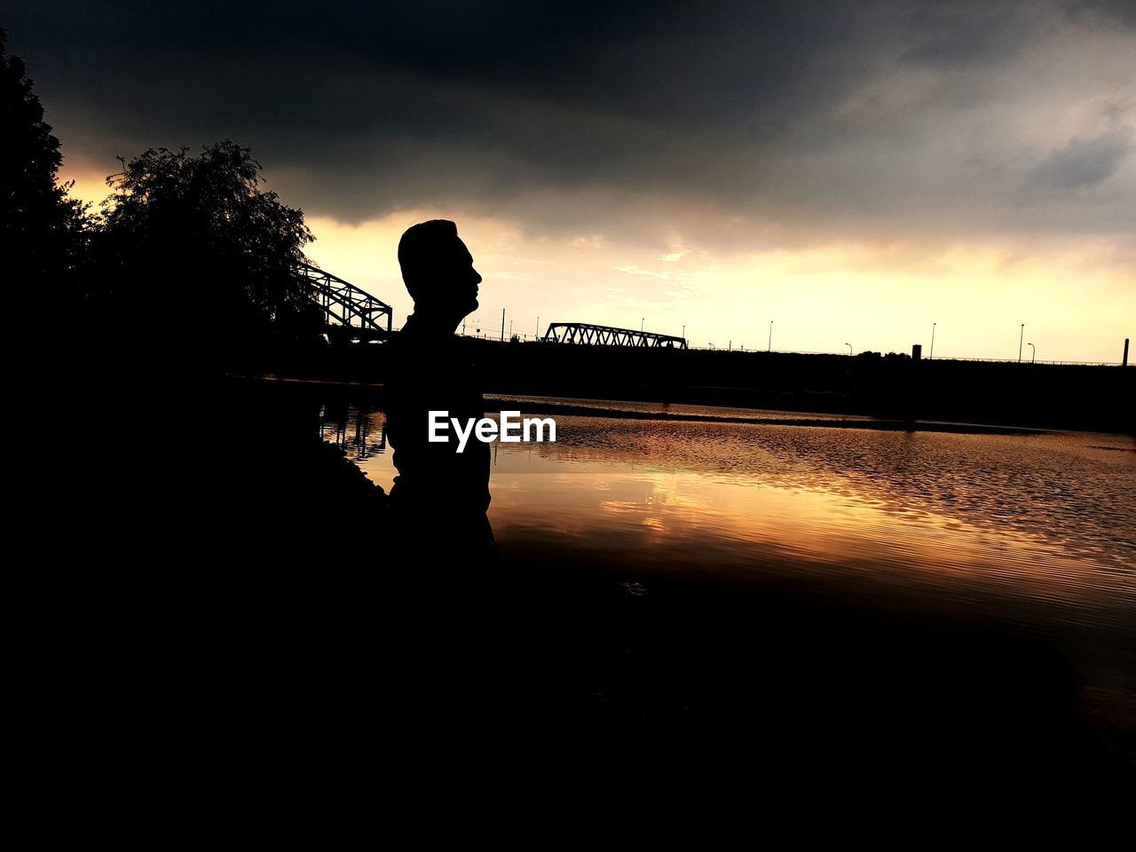 SILHOUETTE MAN STANDING BY BRIDGE AGAINST SKY DURING SUNSET