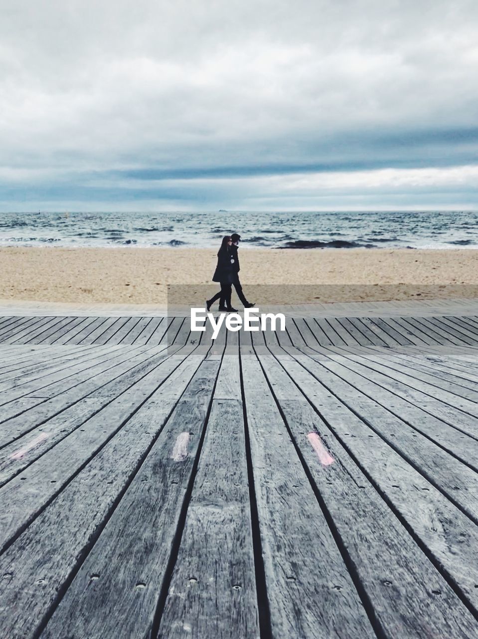 REAR VIEW OF MAN STANDING ON PIER OVER SEA AGAINST SKY