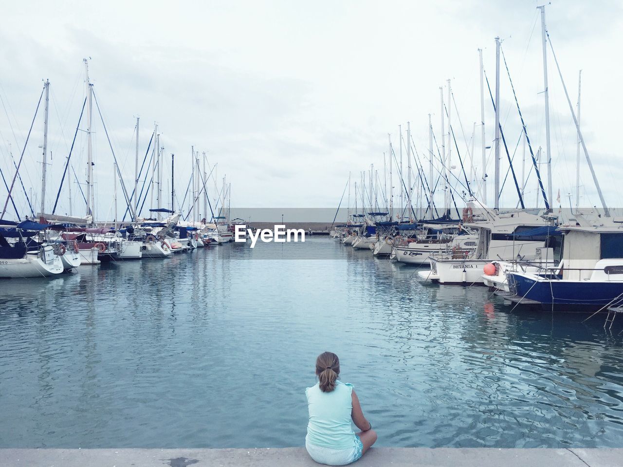 Rear view of woman sitting on pier at harbor