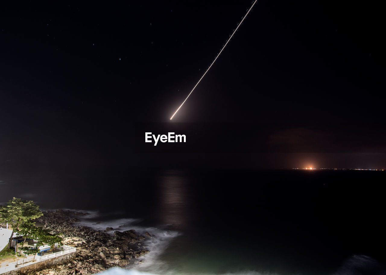 Scenic view of sea against sky with comet at night