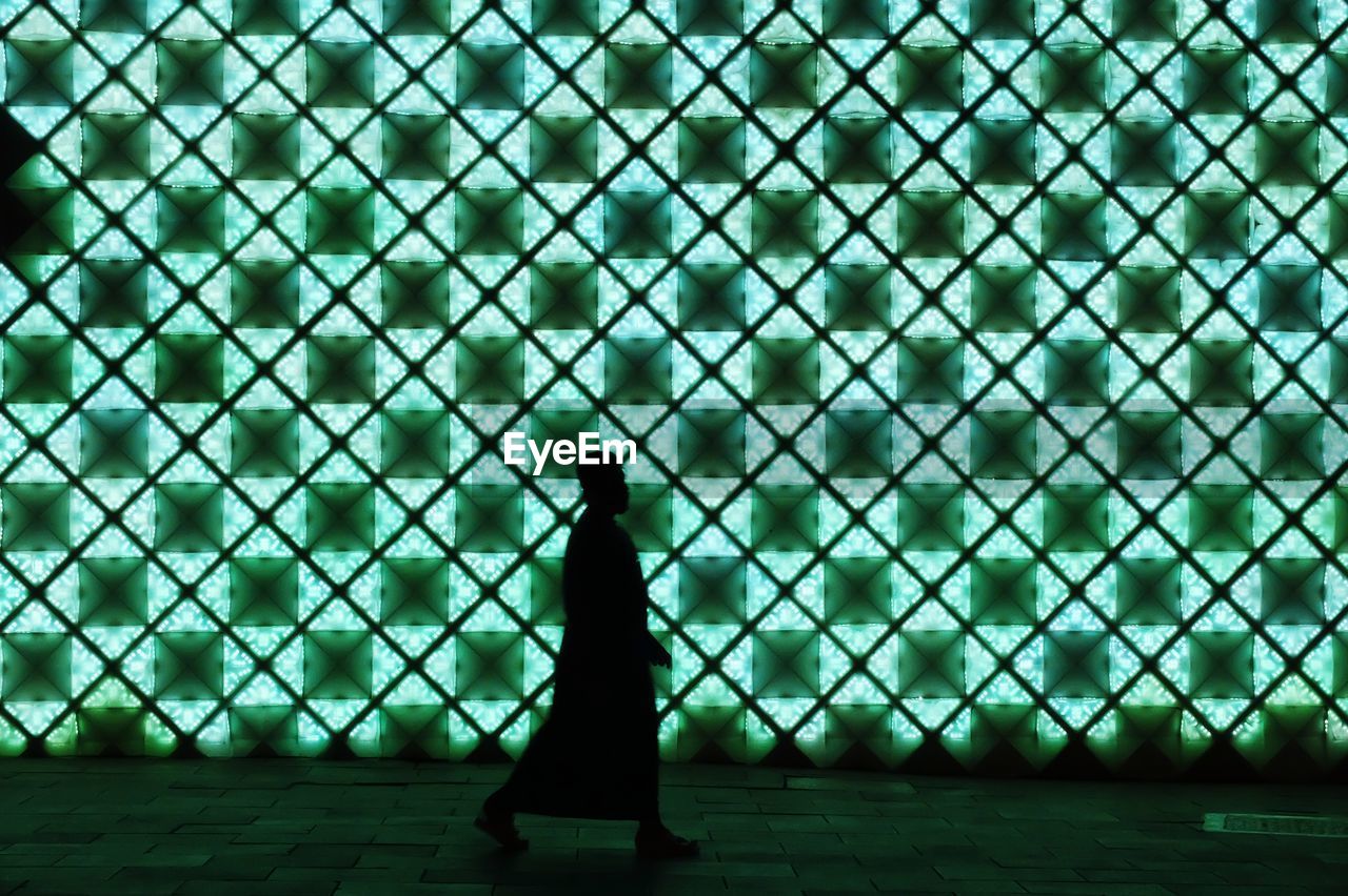 Silhouette man walking against illuminated wall