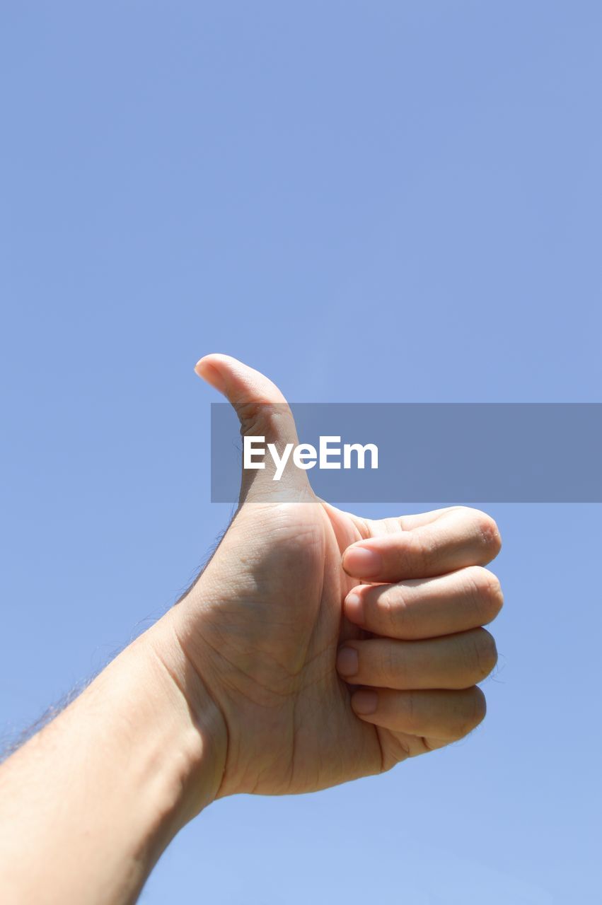 Low angle view of human hand against clear blue sky