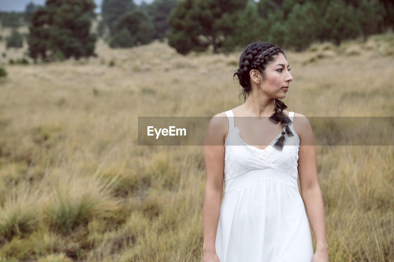 Woman looking away while standing by plants against trees and sky