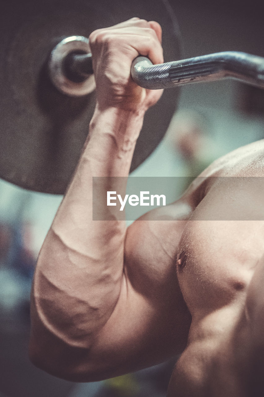 Close-up of shirtless muscular man lifting barbell in gym