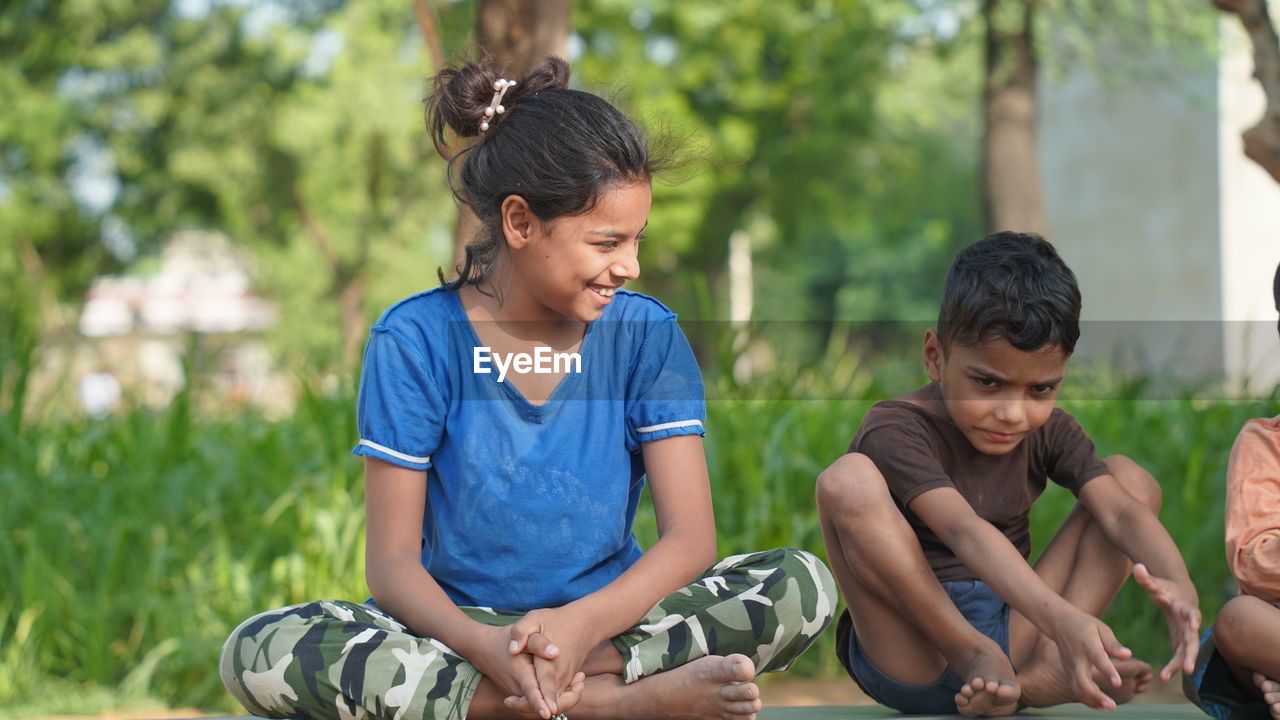 Indian little girl and a boy doing meditate yoga asana on roll mat with eyes closed in park.