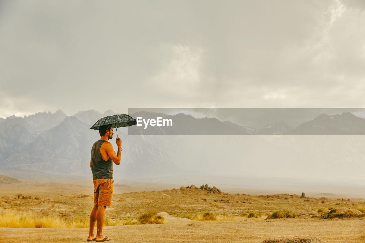 Young man in desert of northern california, holding umbrella in rain.