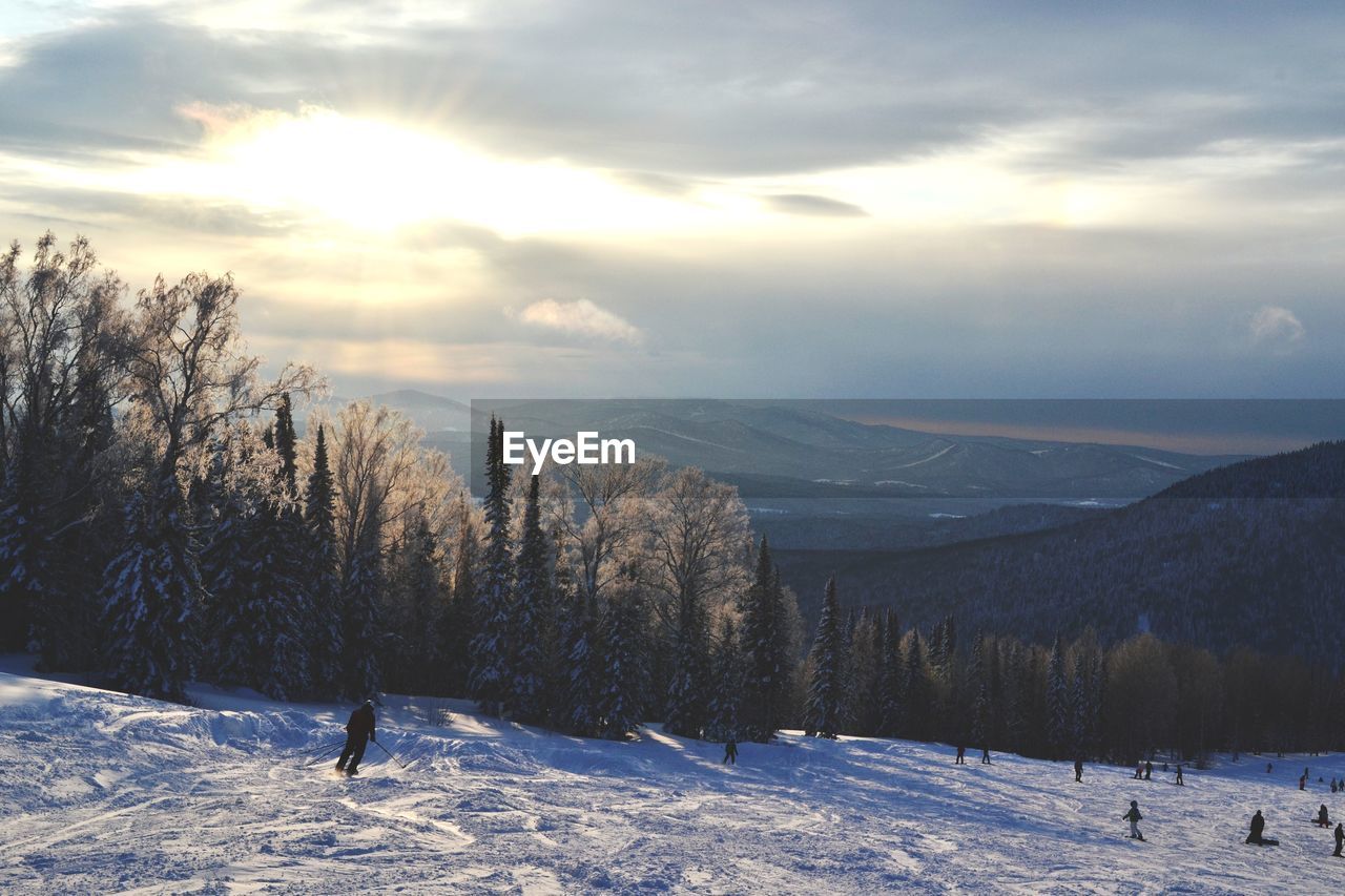 People skiing on snow covered field against sky during sunny day