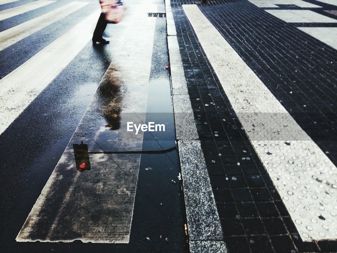 Pedestrian and road signal reflecting in puddle on street