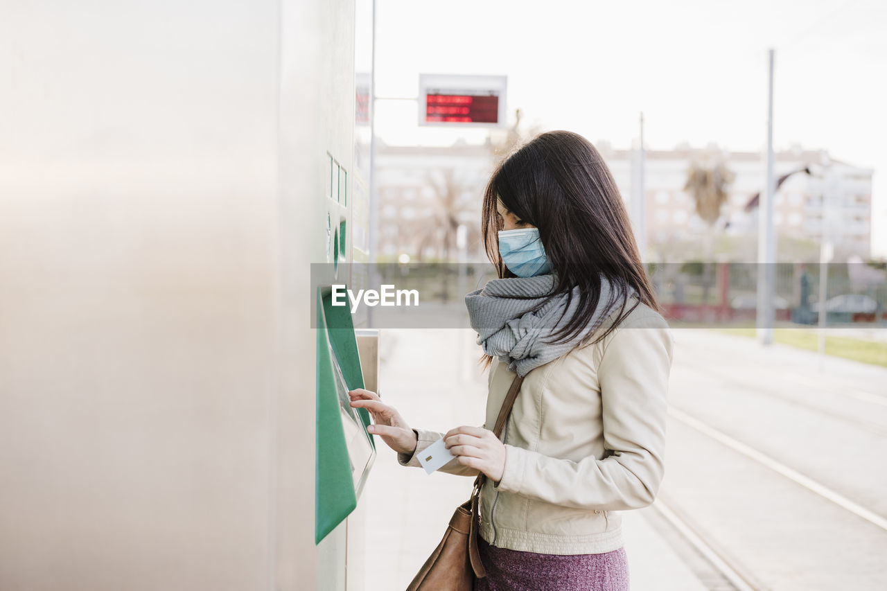 Woman with protective face mask buying ticket at kiosk during covid-19