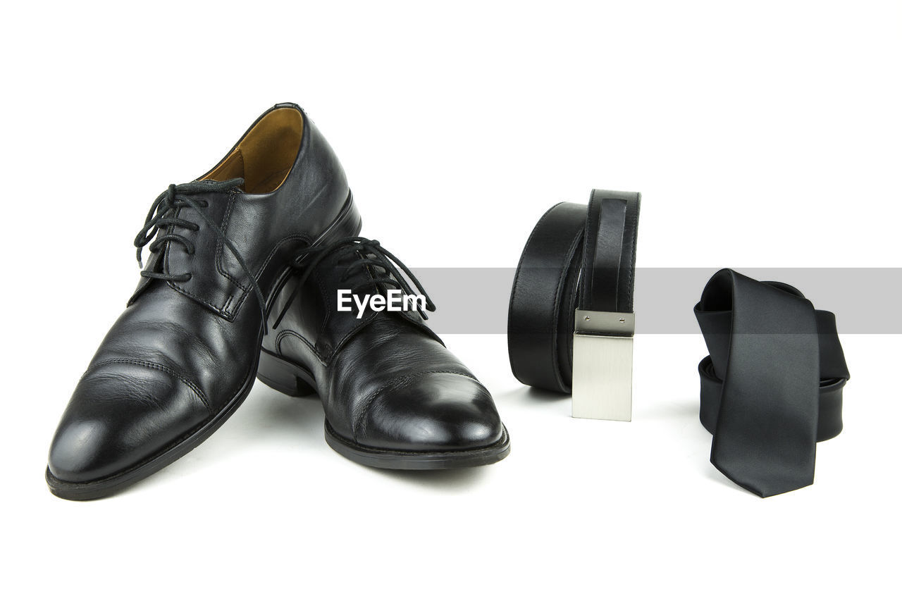 Black shoes by belt and tie against white background