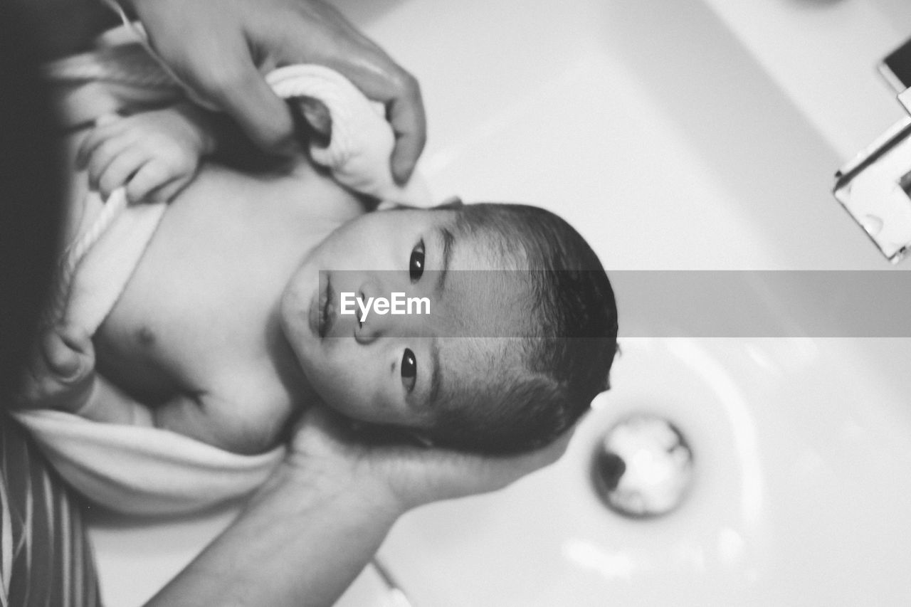 Cropped hands of parent holding newborn son at sink