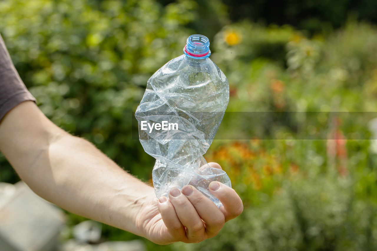 Hand holding crumpled empty plastic bottle in the park