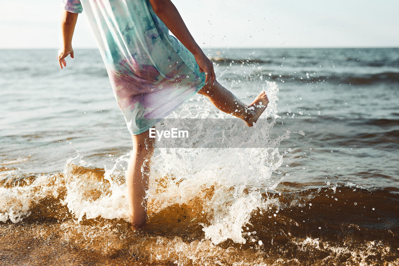 Girl spending a free time jumping splashing in a sea on a beach at sunset during summer vacation