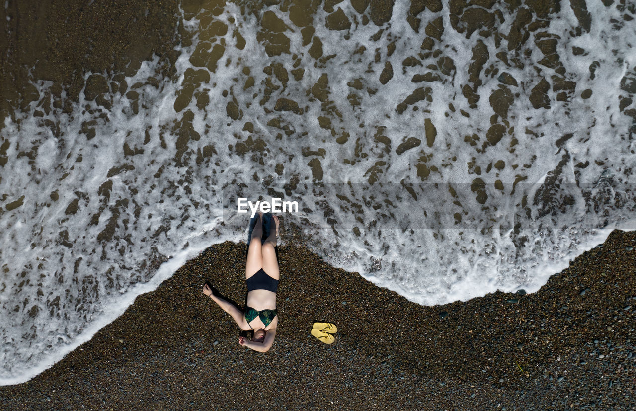 Woman with swimsuit on a sandy beach with braking waves on the shore. aerial drone photograph