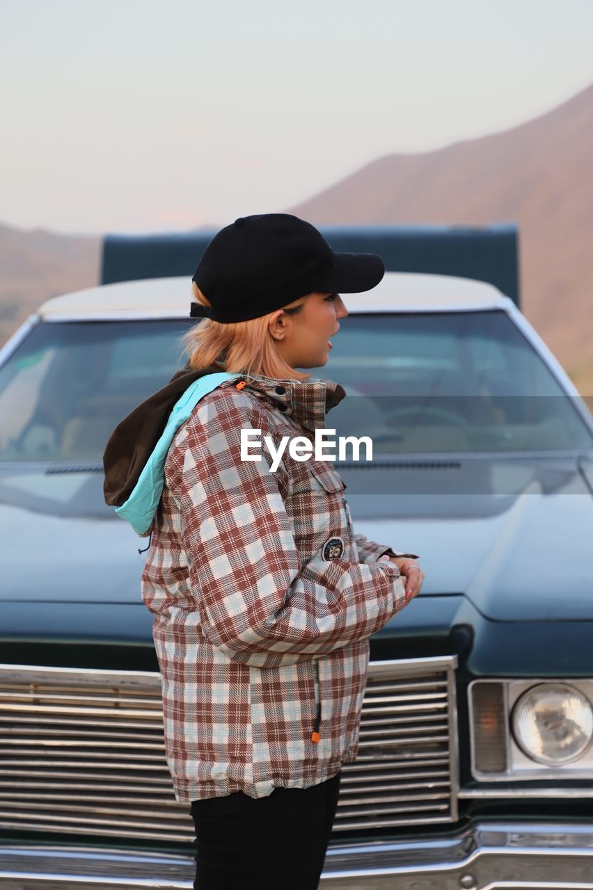 Rear view of a girl standing against car