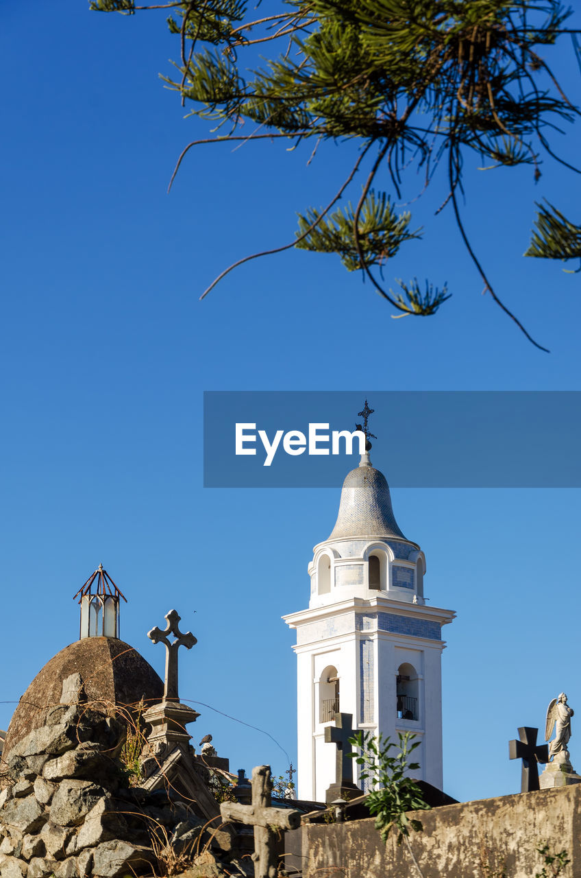 Low angle view of bell tower at cemetery against clear blue sky