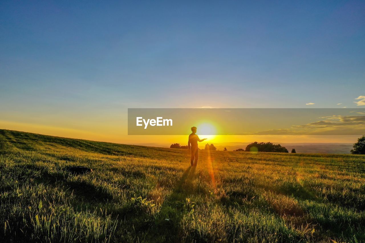 MAN STANDING ON FIELD DURING SUNSET