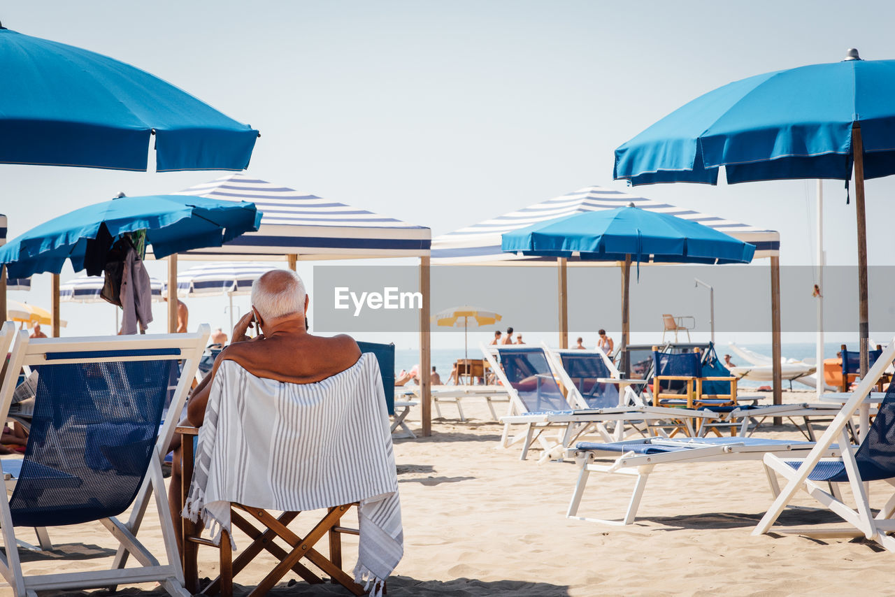 Rear view of senior man sitting on chair at beach