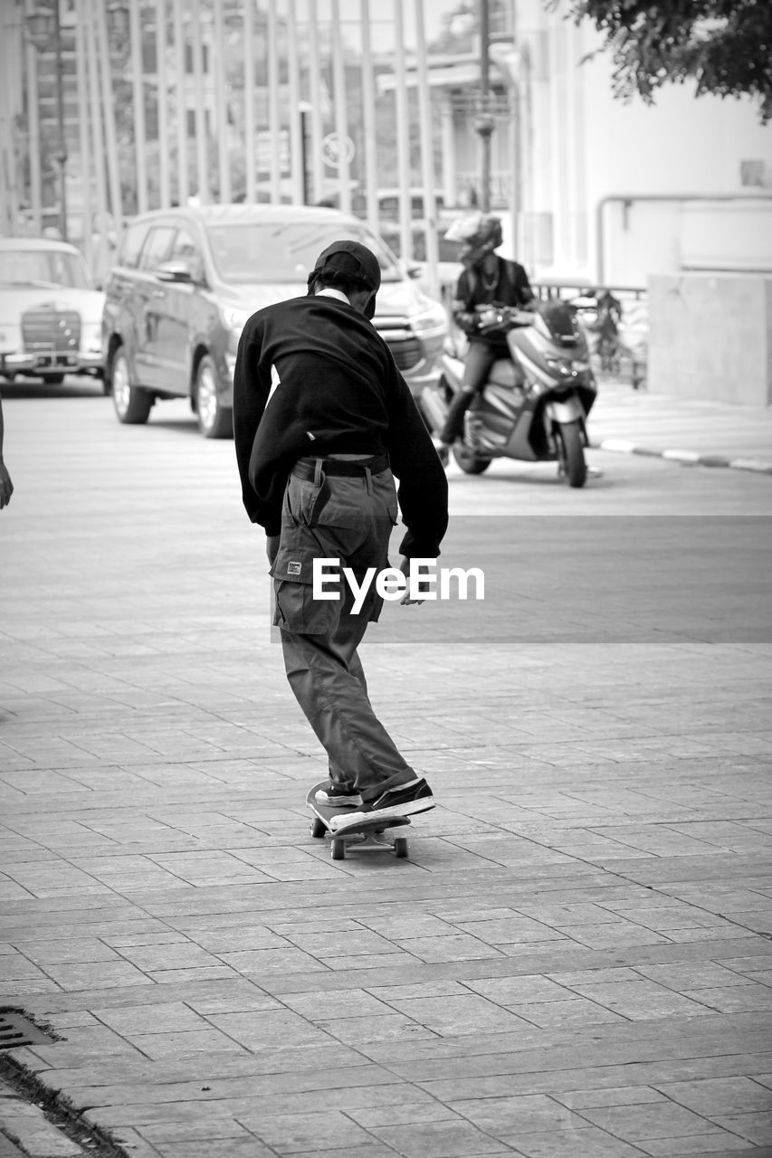 Rear view of men skating on street in city