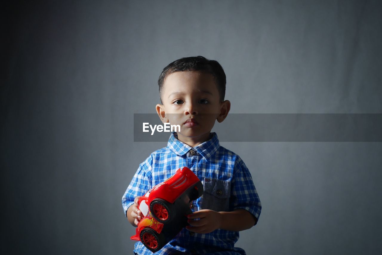 Portrait of boy with toy car against gray background