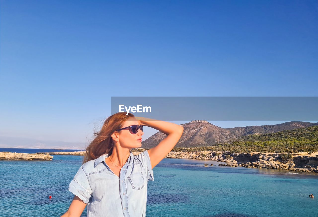 Woman standing by sea against clear blue sky