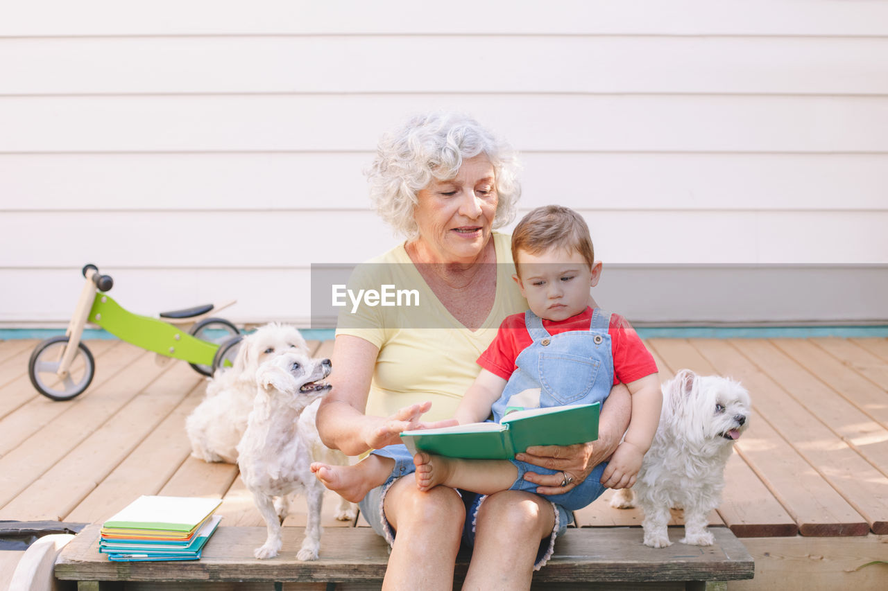 Happy senior woman sitting with grandson and dog outdoors